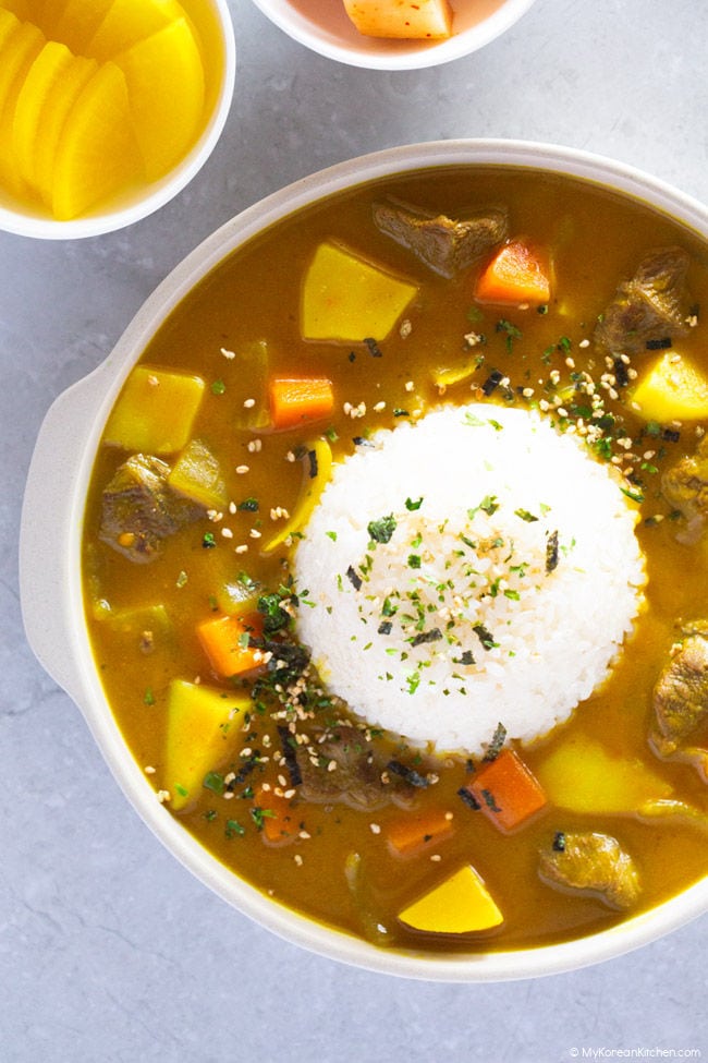 Korean curry is presented encircling a mound of rice in a ribbed plate.