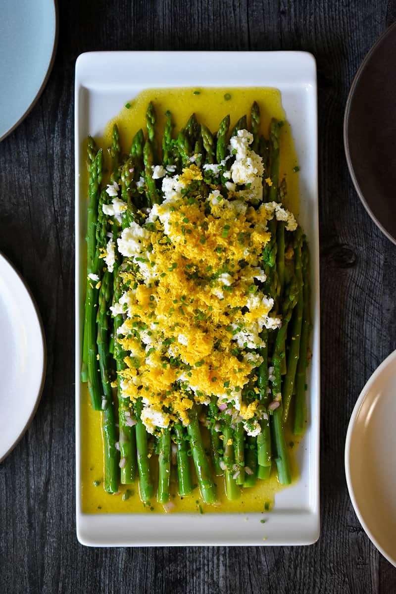 An overhead shot of a rectangular plate filled with Asparagus Mimosa, cooked asparagus tossed with a lemon vinaigrette and topped with chopped hard boiled eggs and chives.