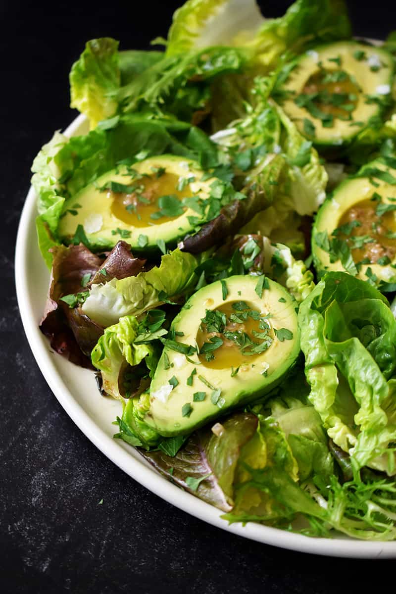 A side shot of avocado salad with garlic anchovy vinaigrette and topped with fresh herbs