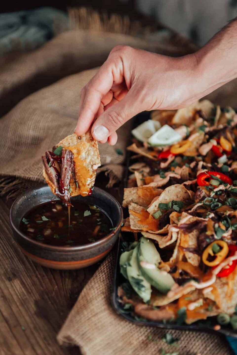 A person dipping birria nachos into a dipping sauce.