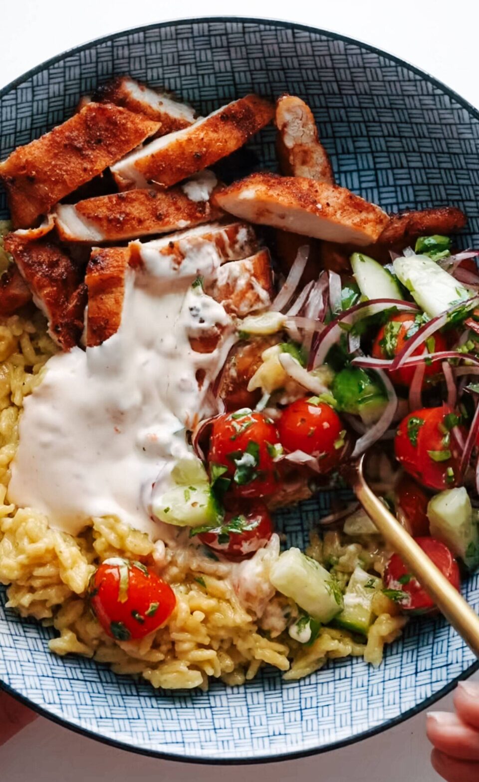 Bowl with seasoned chicken, rice, cucumber salad, and a calabrian chili sauce.