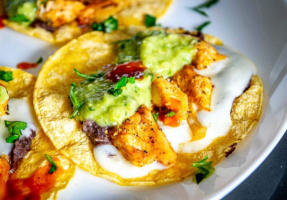 Close up of Chicken Taco drenched in Avocado Salsa Verde, freshly chopped cilantro, and a few drops of hot sauce