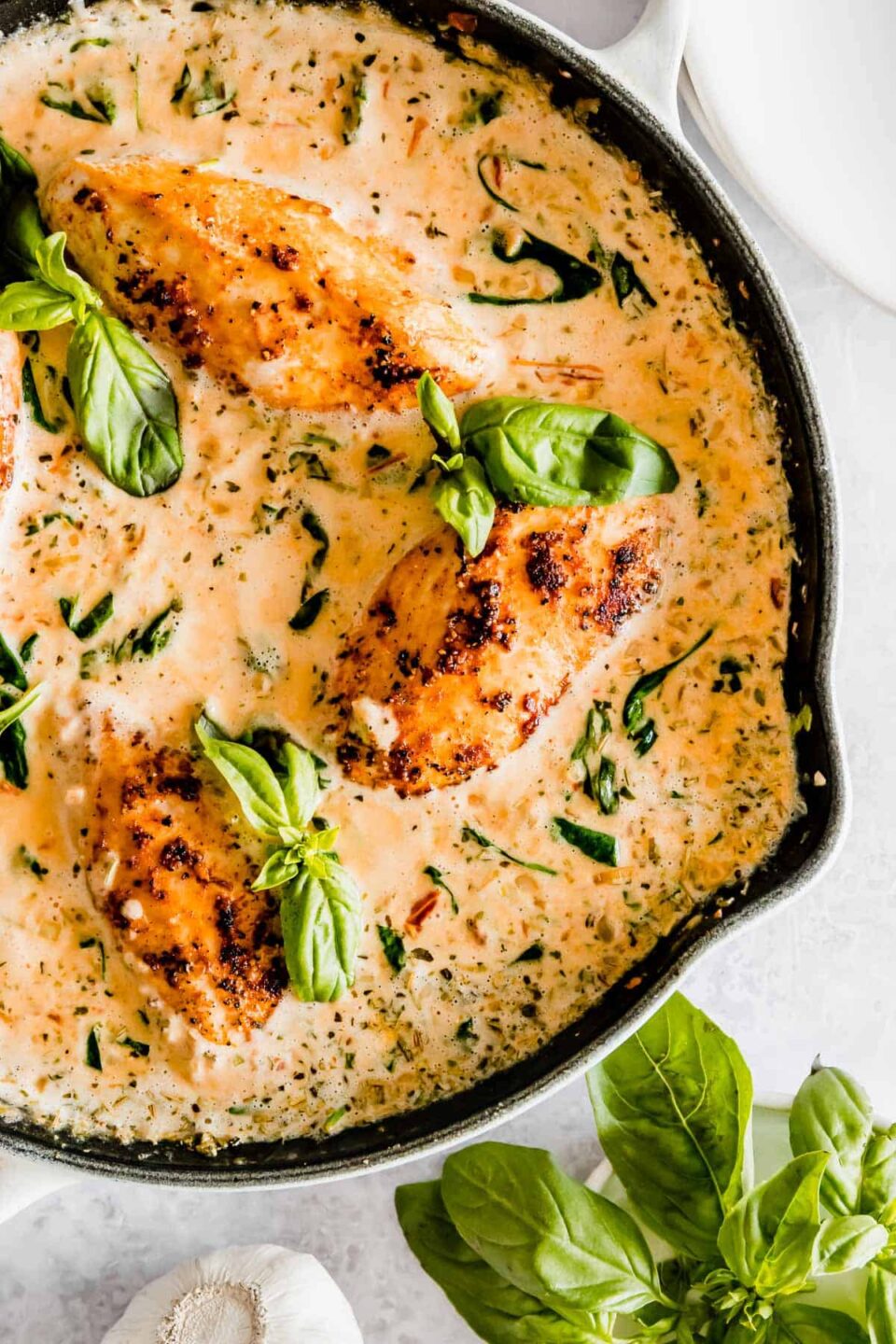 Sautéed chicken breasts in a creamy sauce garnished with basil leaves, served in a skillet.