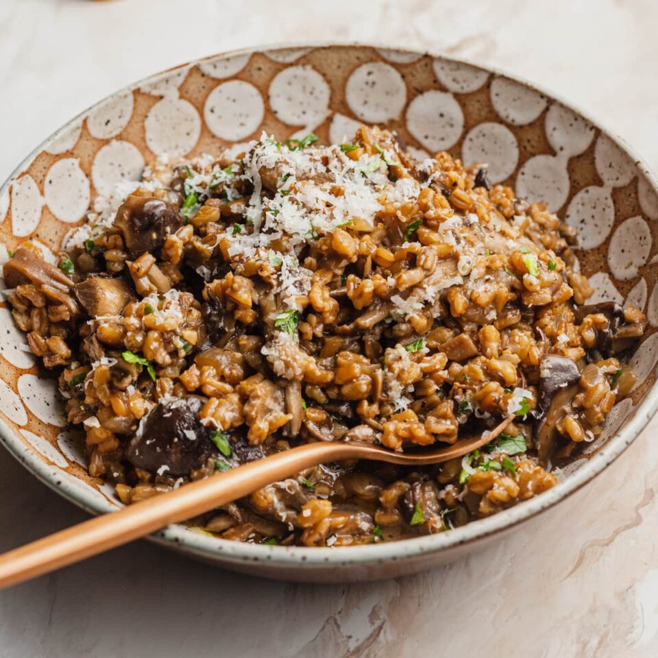 A bowl of farro topped with parmesan cheese, fresh herbs, and a bronze spoon.