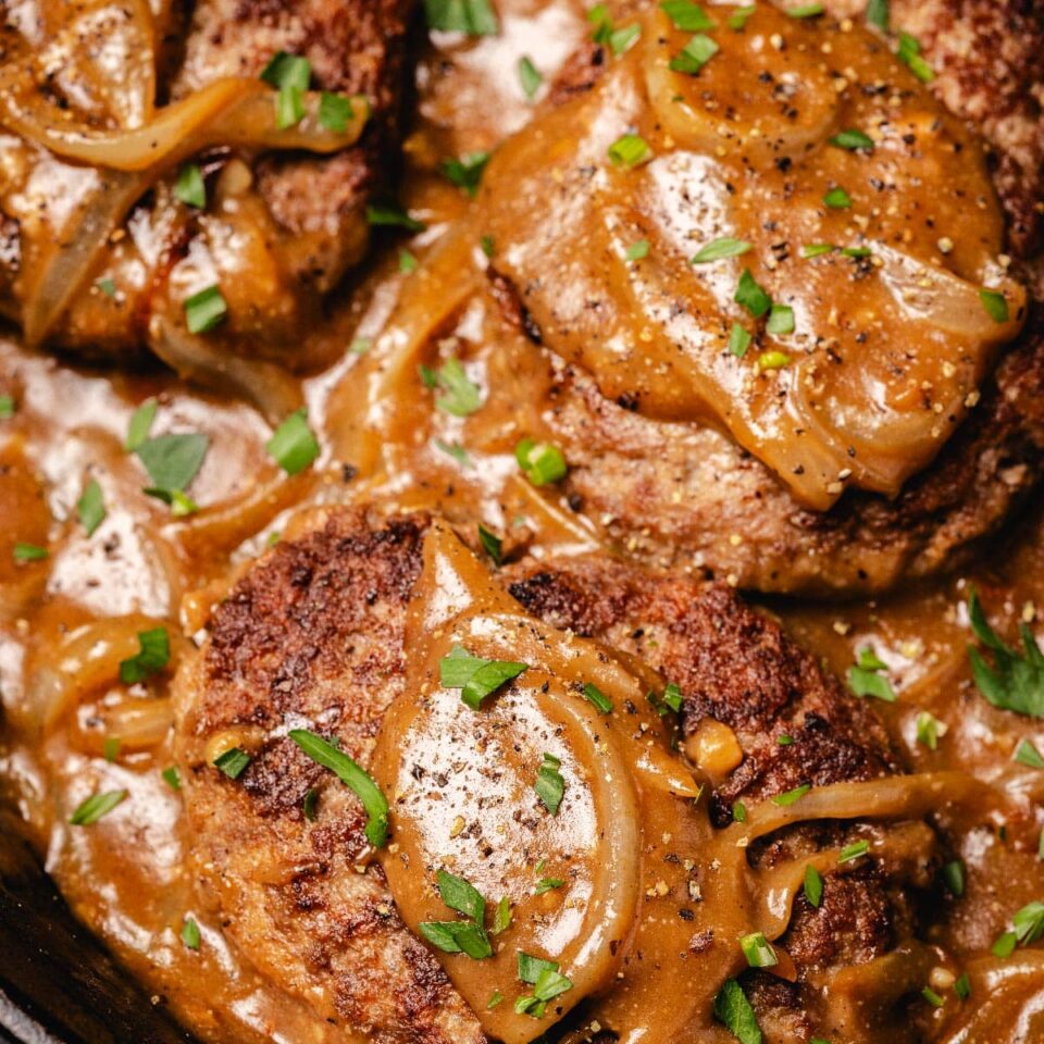 Hamburger steaks in onion gravy in cast iron skillet.