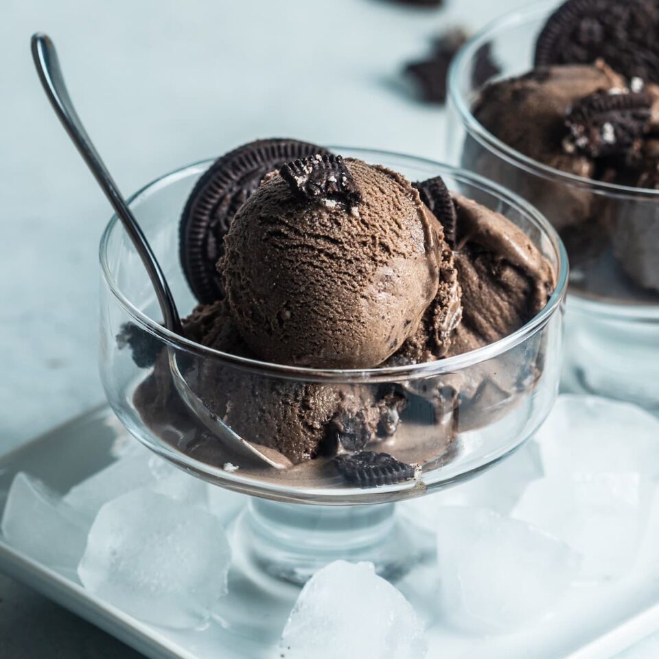 Oreo ice cream scoops in a glass bowl with a spoon and crushed oreo cookies.