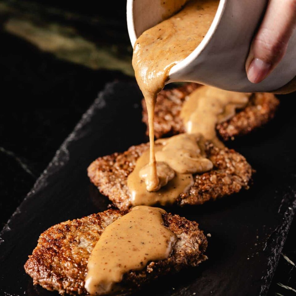 Graving in white cup being poured onto cube steaks on serving platter.