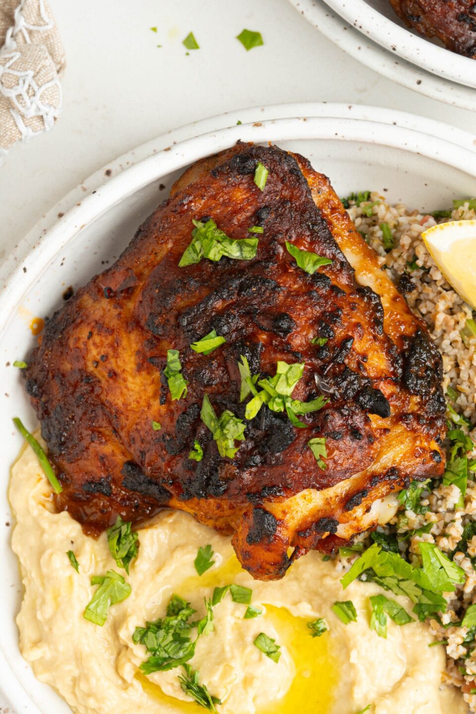 a bowl with a chicken thigh, hummus, and salad