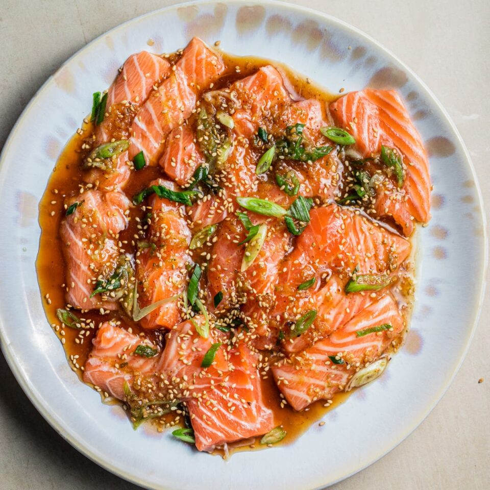 Plate of salmon crudo with a soy-citrus dressing topped with scallions and sesame seeds.