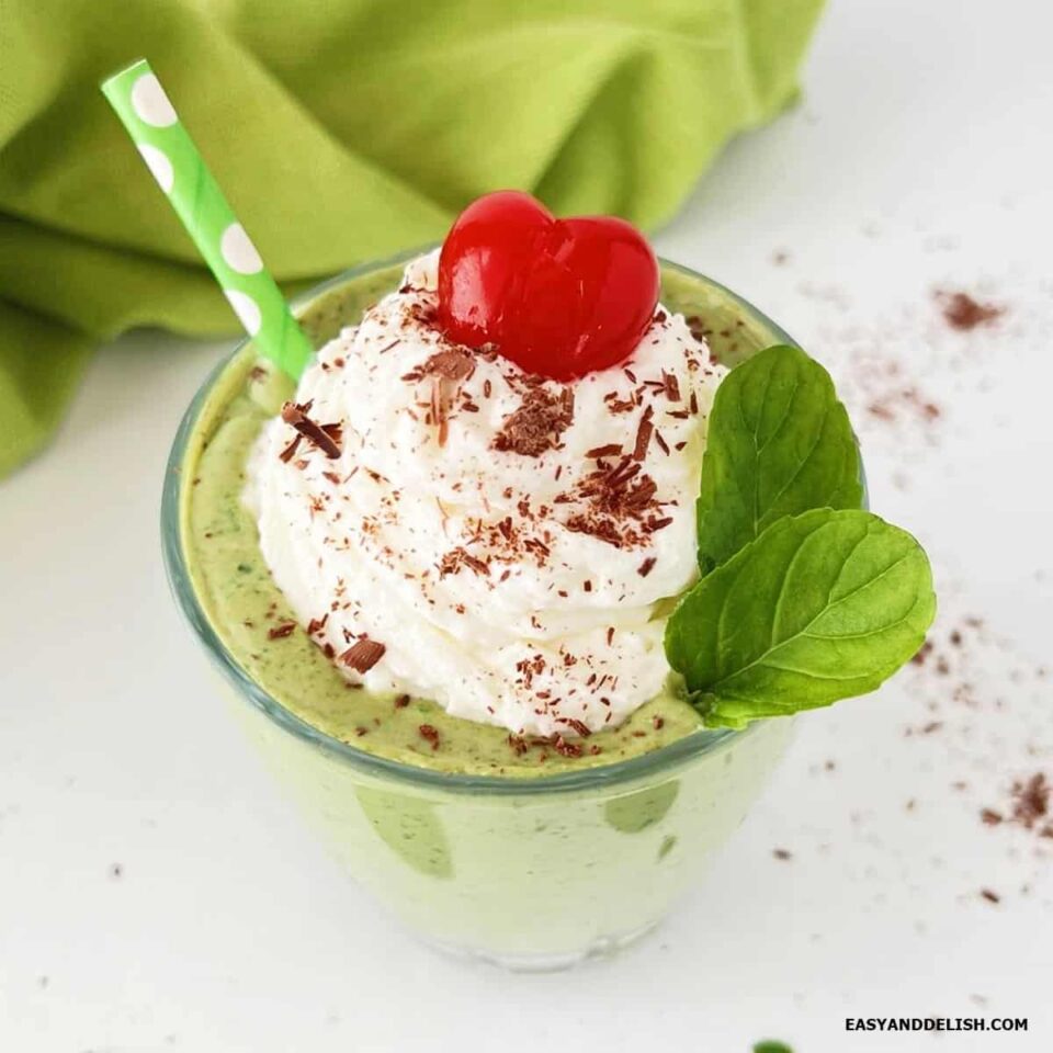 A glass of homemade shamrock protein shake topped with whipped cream, chocolate shavings, and a cherry.