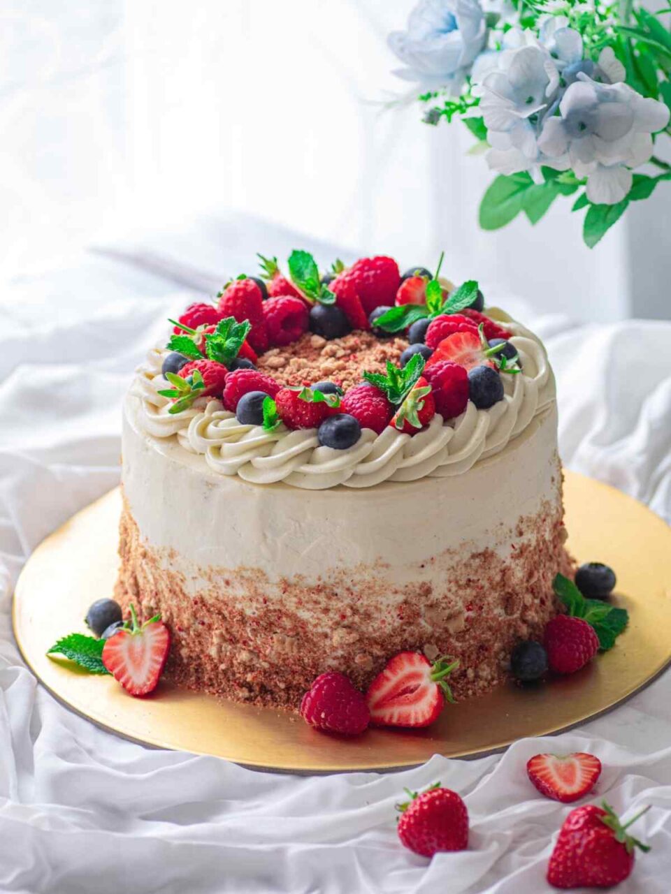 Strawberry cheesecake cake decorated with berries on golden platter and white background