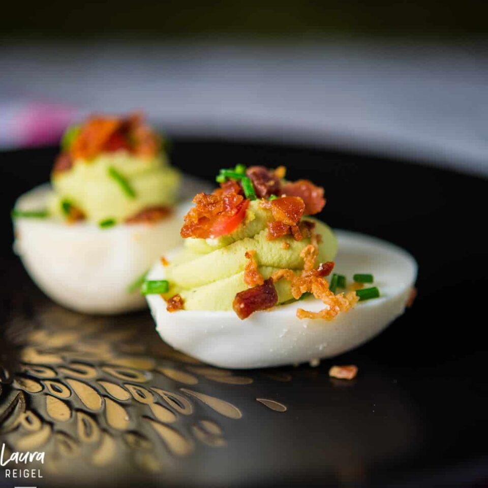 Avocado deviled eggs with crispy bacon, fresh tomatoes and chives.