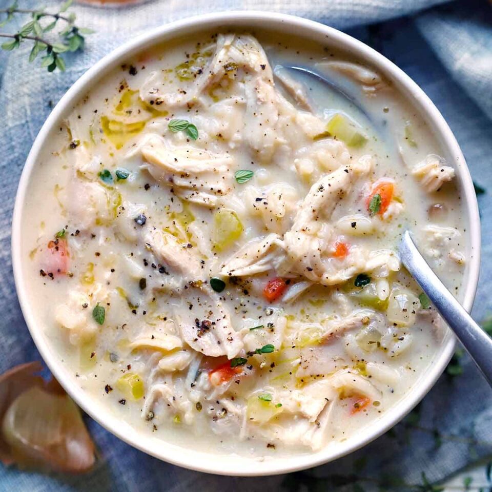 Square photo of creamy chicken and rice soup in a white bowl, overhead view, with a spoon.