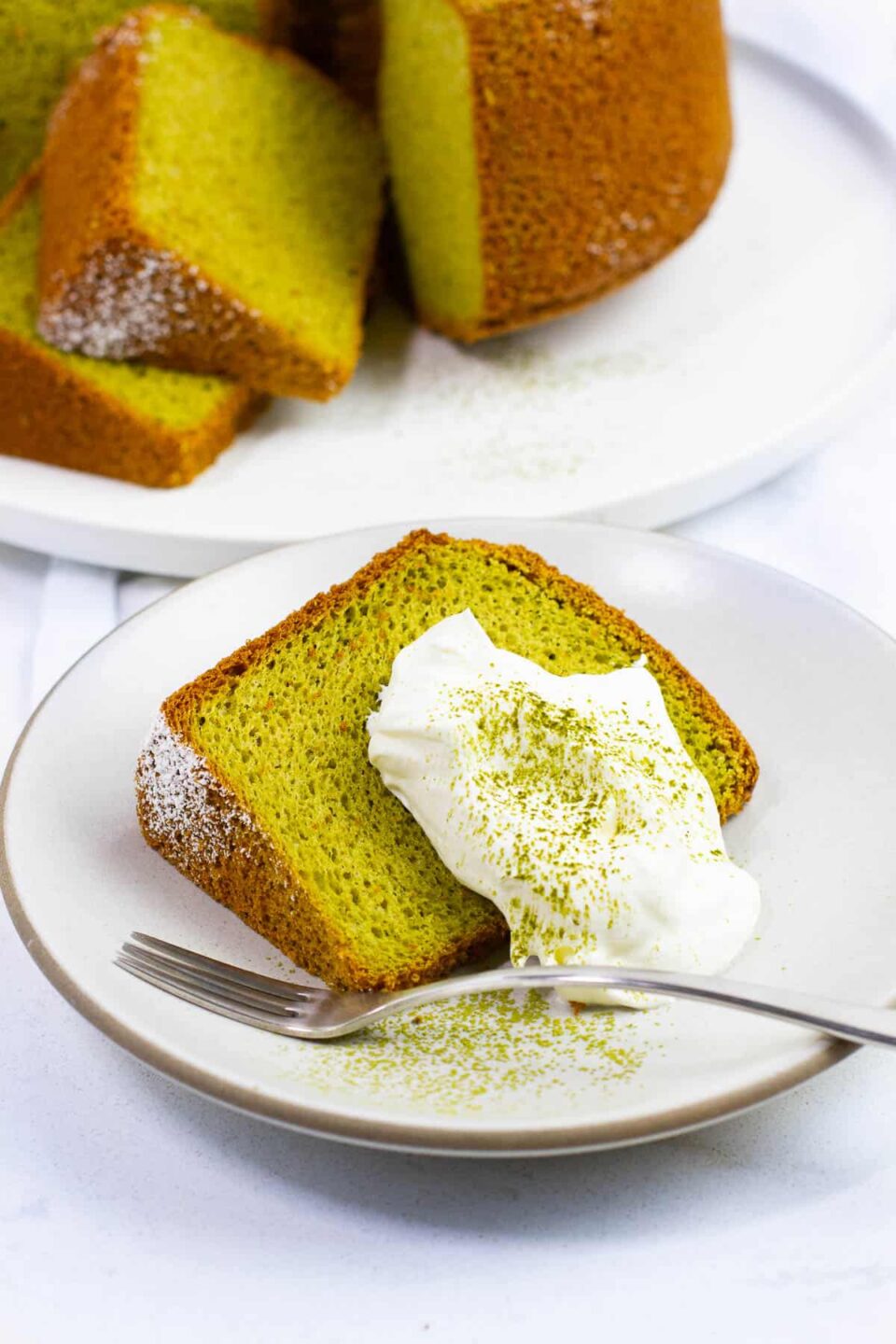 A slice of matcha chiffon cake with whipped cream topping.