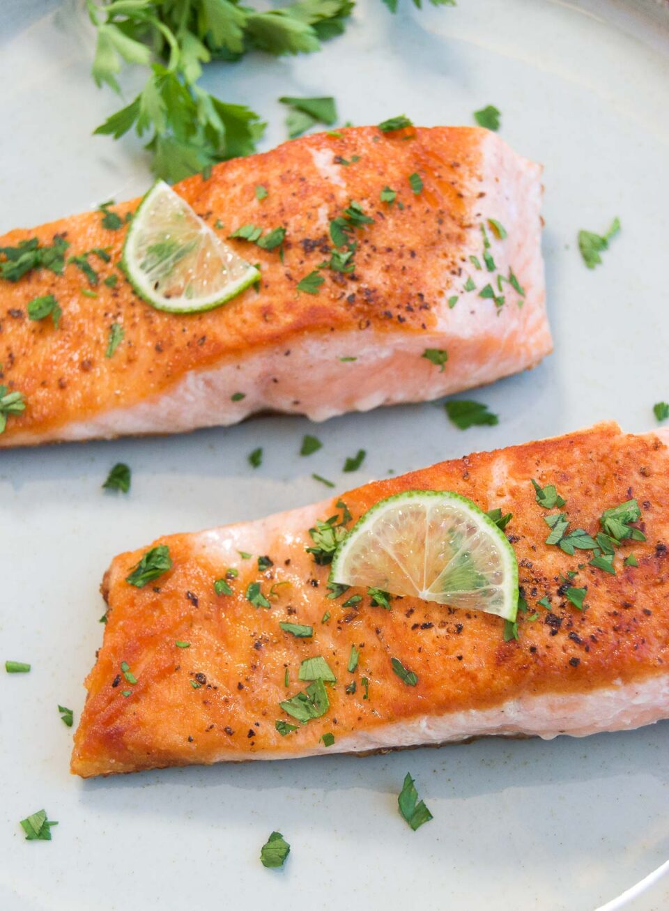 two pieces of seared salmon on a plate garnished with lemon and fresh chopped herbs