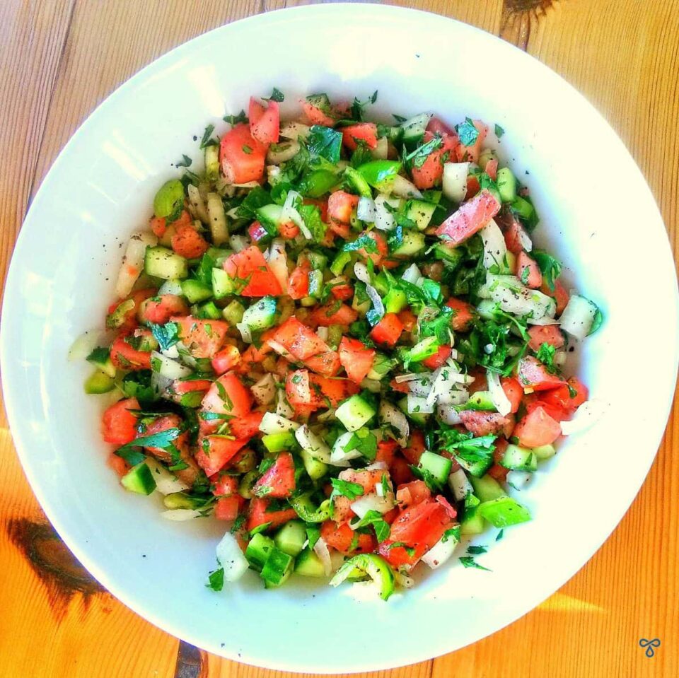 A bowl of finely chopped salad taken from above. Peppers, tomatoes, onion and cucumber are visible.