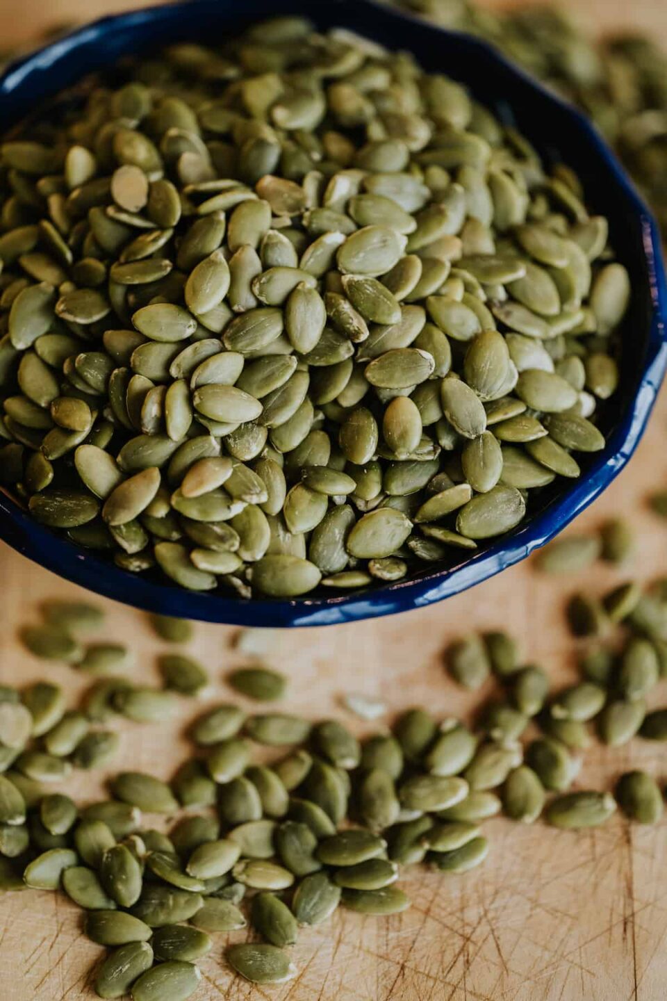 closeup shot of a blue scalloped bowl with raw pepitas on a wooden cutting board.