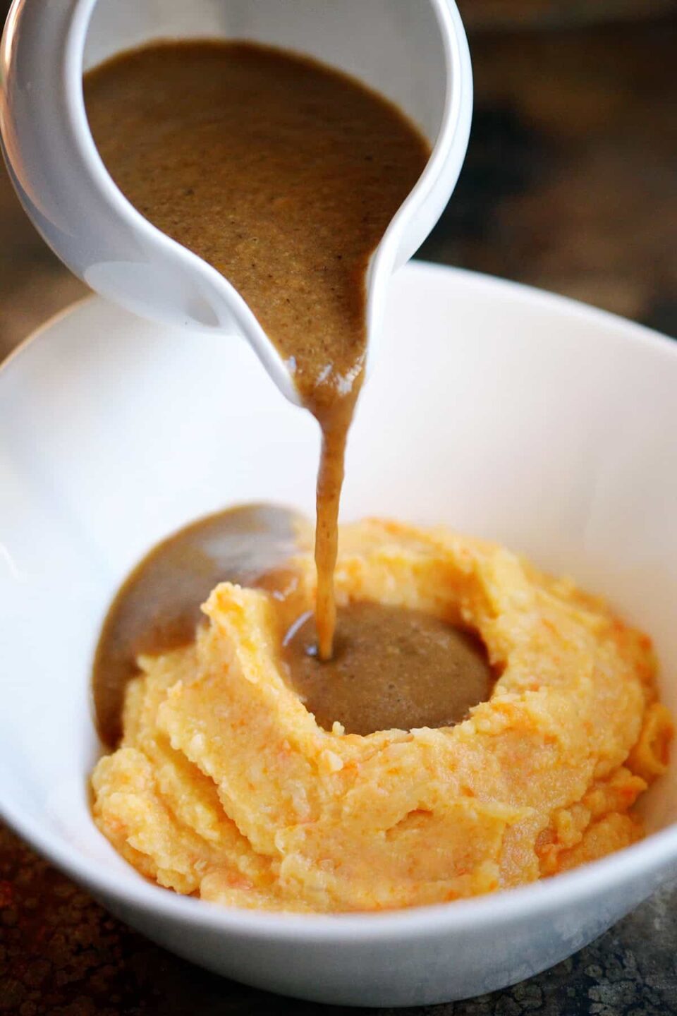 Pouring a gluten free gravy from a gravy boat onto a bowl filled with an orange root vegetable mash.