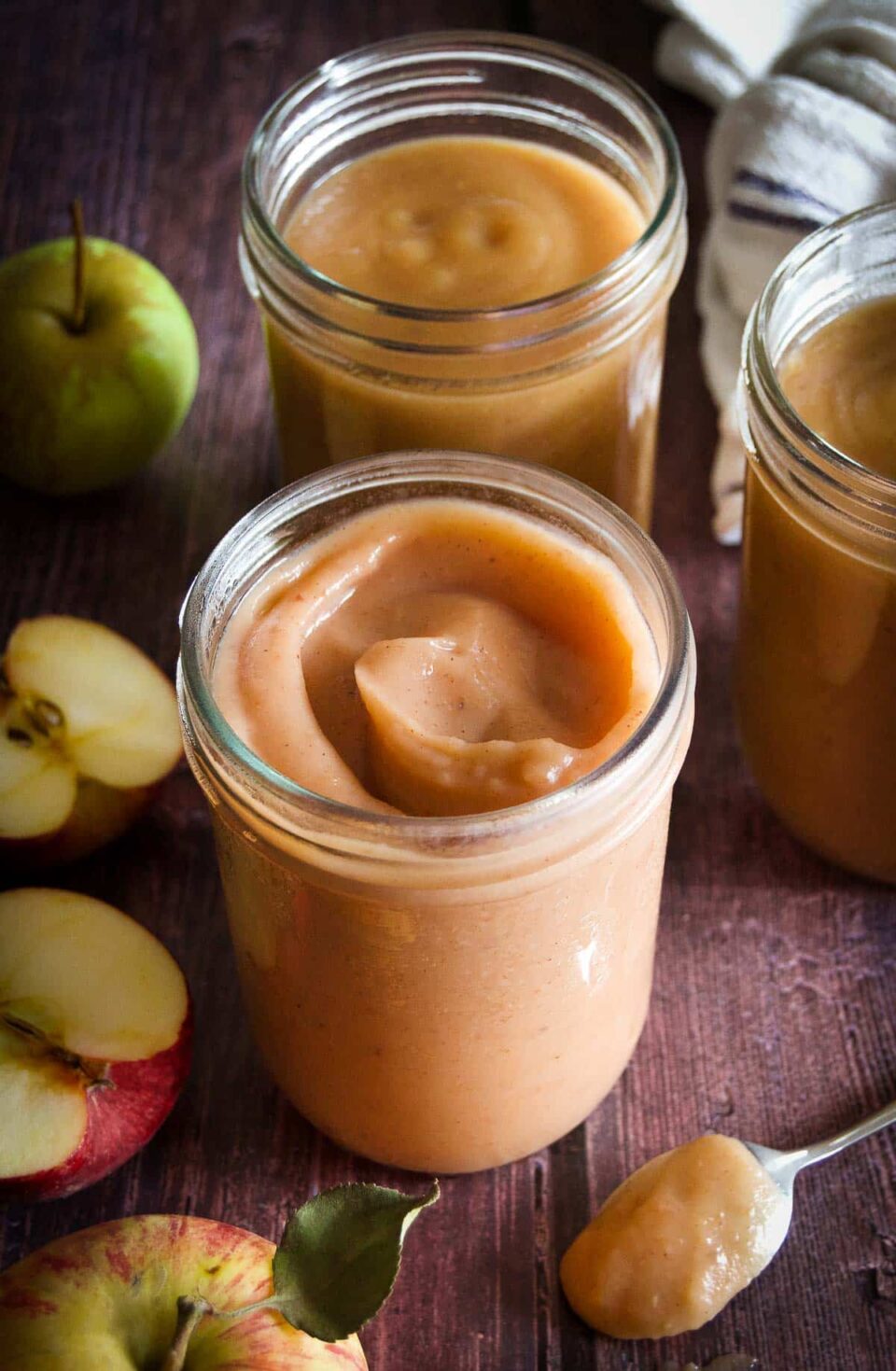 two jars of caramel apple butter from the side on a wooden surface next to halved and whole apples