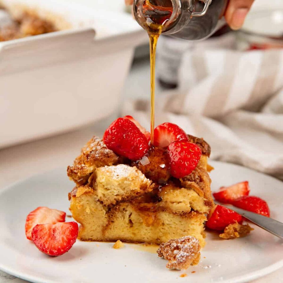 Pouring maple syrup over a slice of brioche french toast casserole with cinnamon toast croutons.