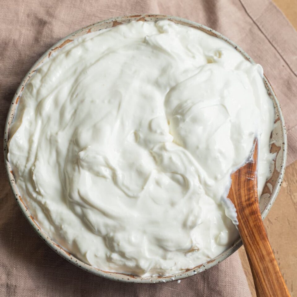 A ceramic bowl filled with Greek yogurt with a wooden spoon in it.