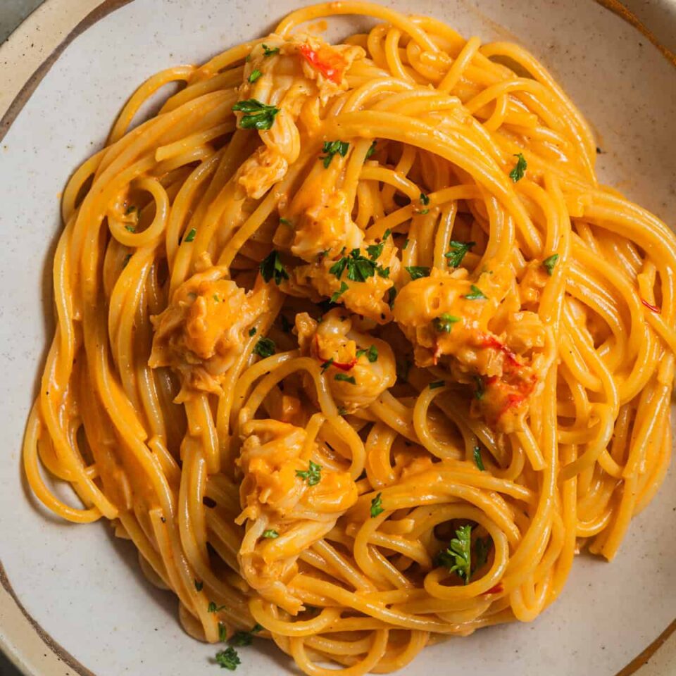 A bowl of pasta in an orange cream sauce topped with bits of lobster and garnished with parsley.