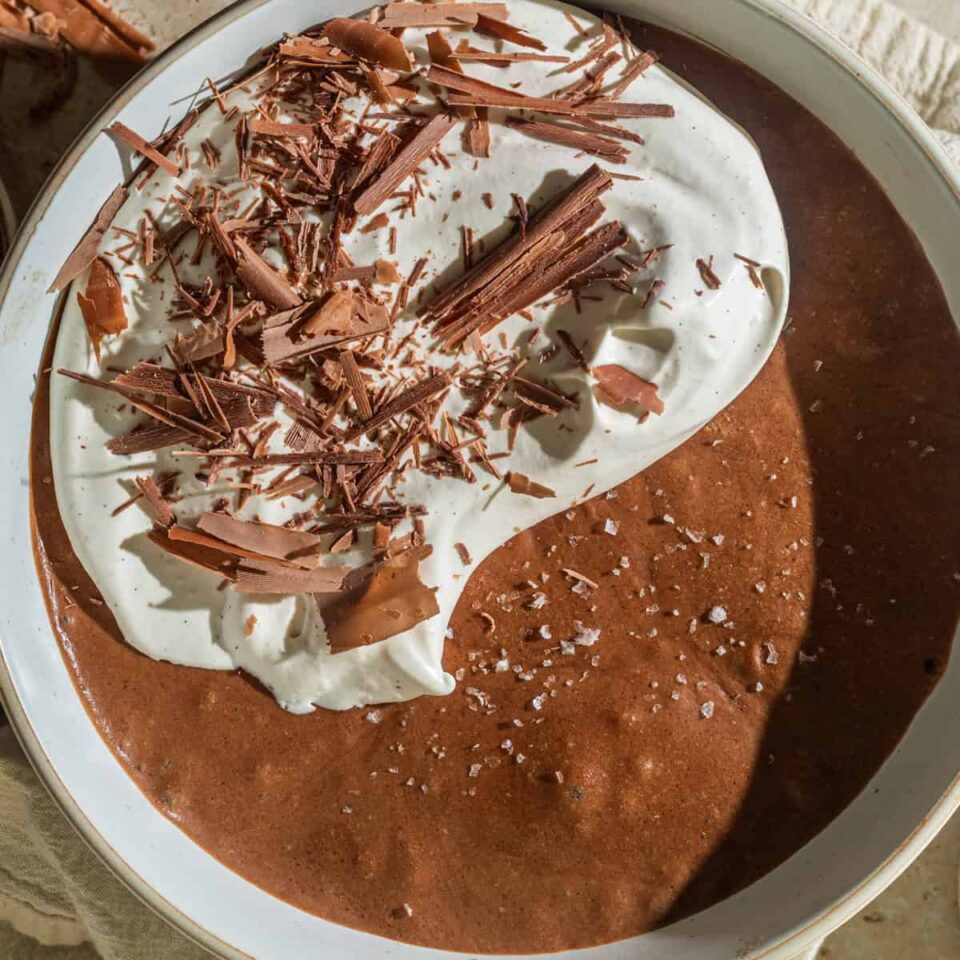 A large bowl of chocolate mousse topped with flaky sea salt, whipped cream, and chocolate shavings.