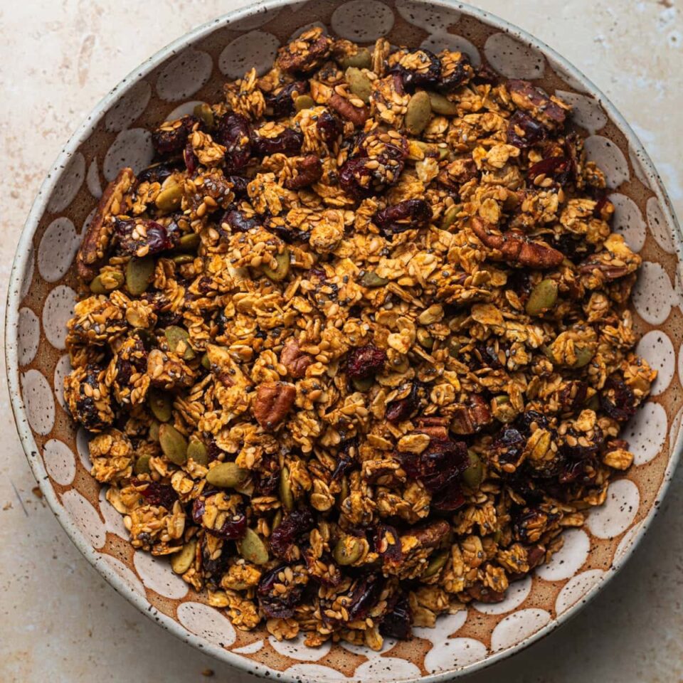 A decorative bowl with granola dotted with pecans, cranberries, and pumpkin seeds.