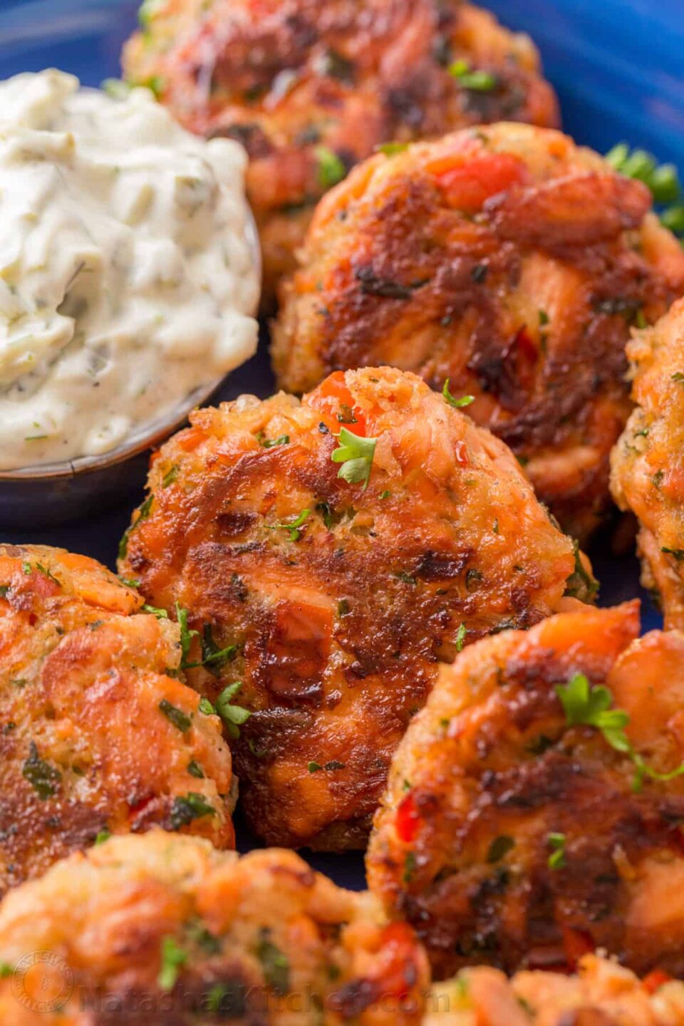 close up picture of salmon patties on a blue plate with tartar sauce for dipping