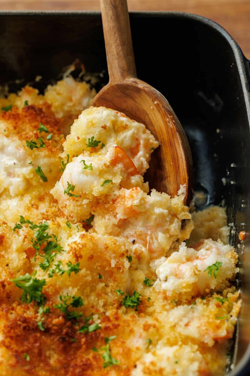 Wooden spoon scooping shrimp casserole out of a dish