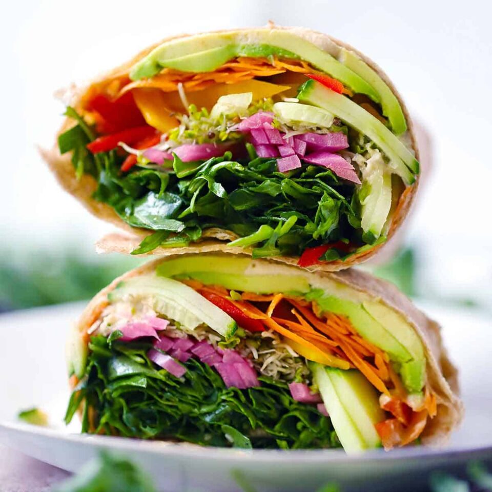 Square photo of a vegan veggie wrap cut in half and stacked on a white plate.