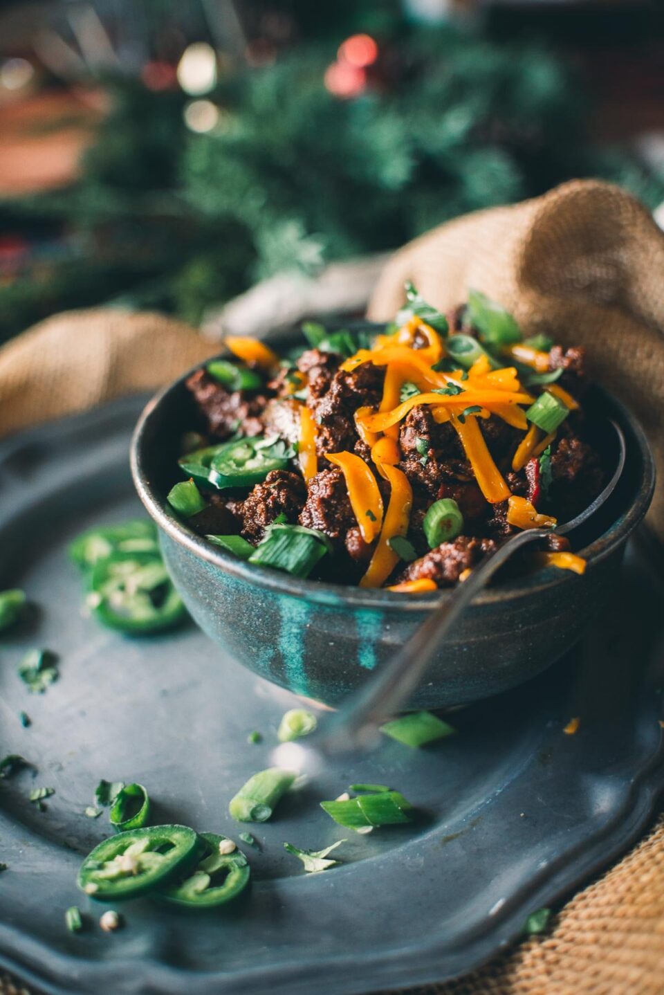 A bowl of venison chili topped with sliced green onions and shredded cheese, garnished with jalapeño slices.