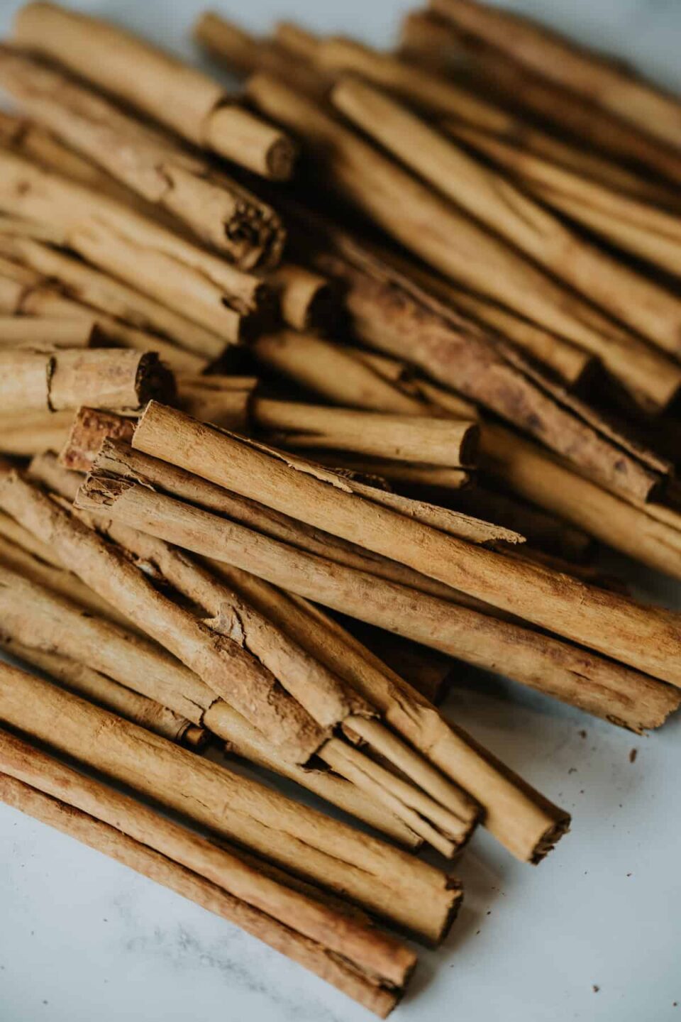 pile of Mexican cinnamon canela sticks on a white and grey marble table; there are some crumbs from the soft bark that have fallen around them.