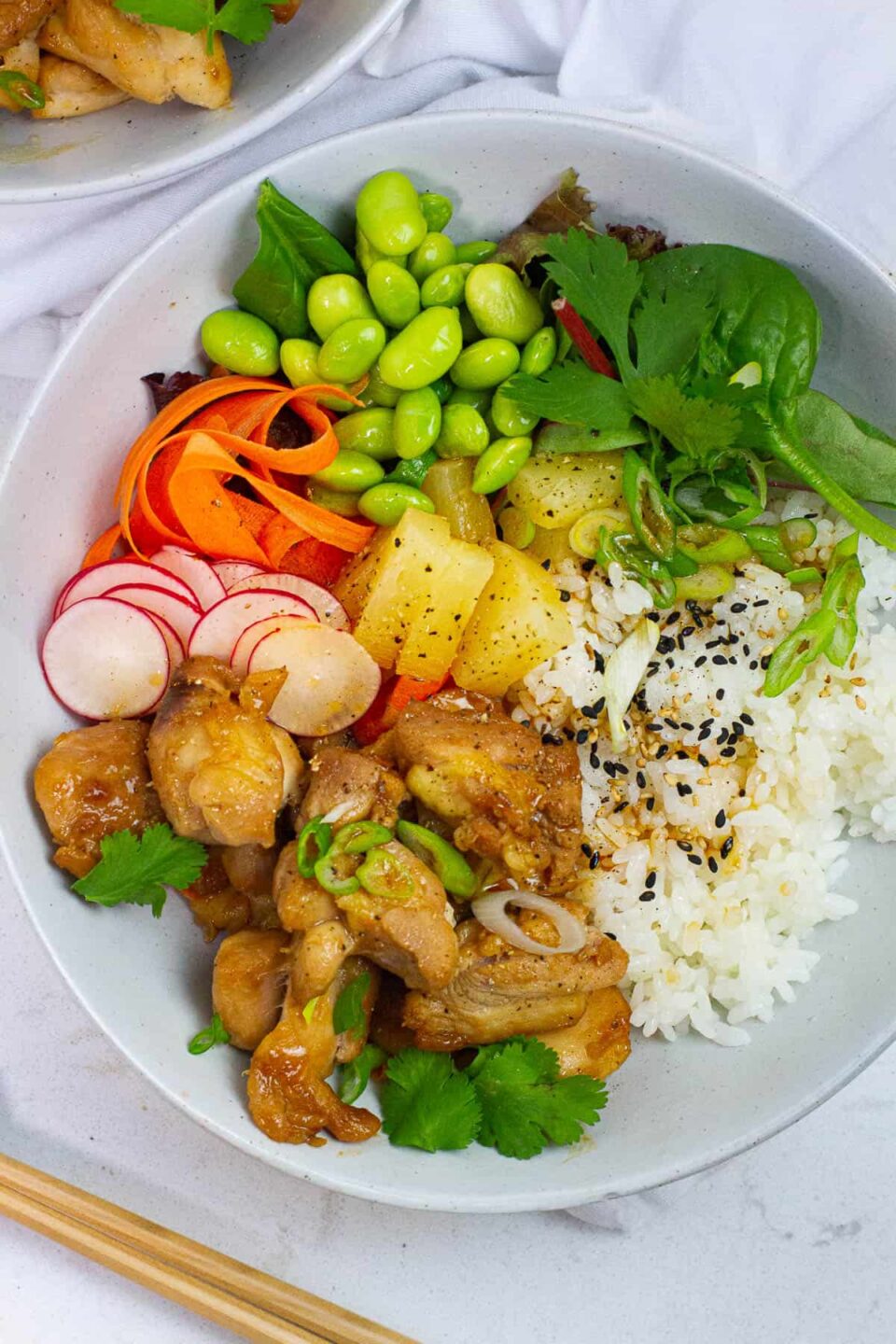 Top view of a chicken poke bowl with radish, carrots, edamame toppings.