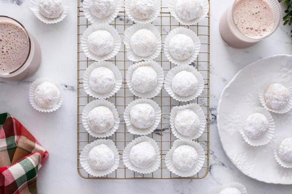 Overhead view of snowball cookies in white mini cupcake liners on a wire rack.