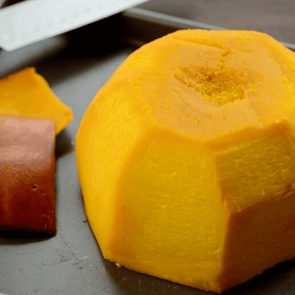 A peeled pumpkin cut in half in a tray with a knife on the side.