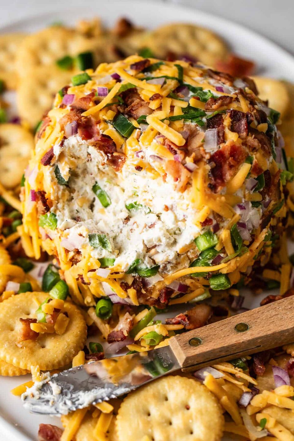 An easy jalapeño cheese ball covered with bacon and cheddar on a plate with crackers.