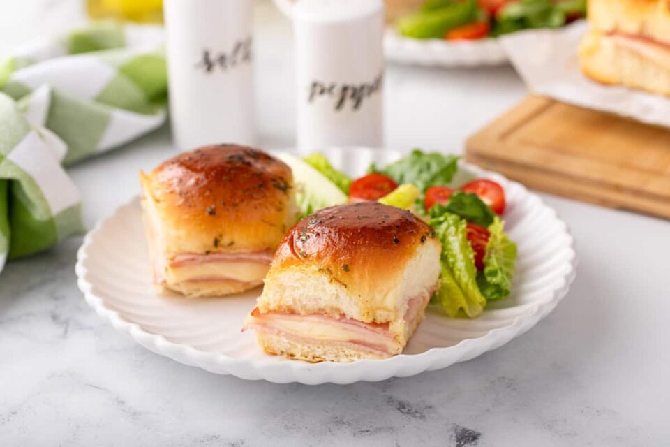 Two hot ham and cheese sliders next to a garden salad on a white plate.