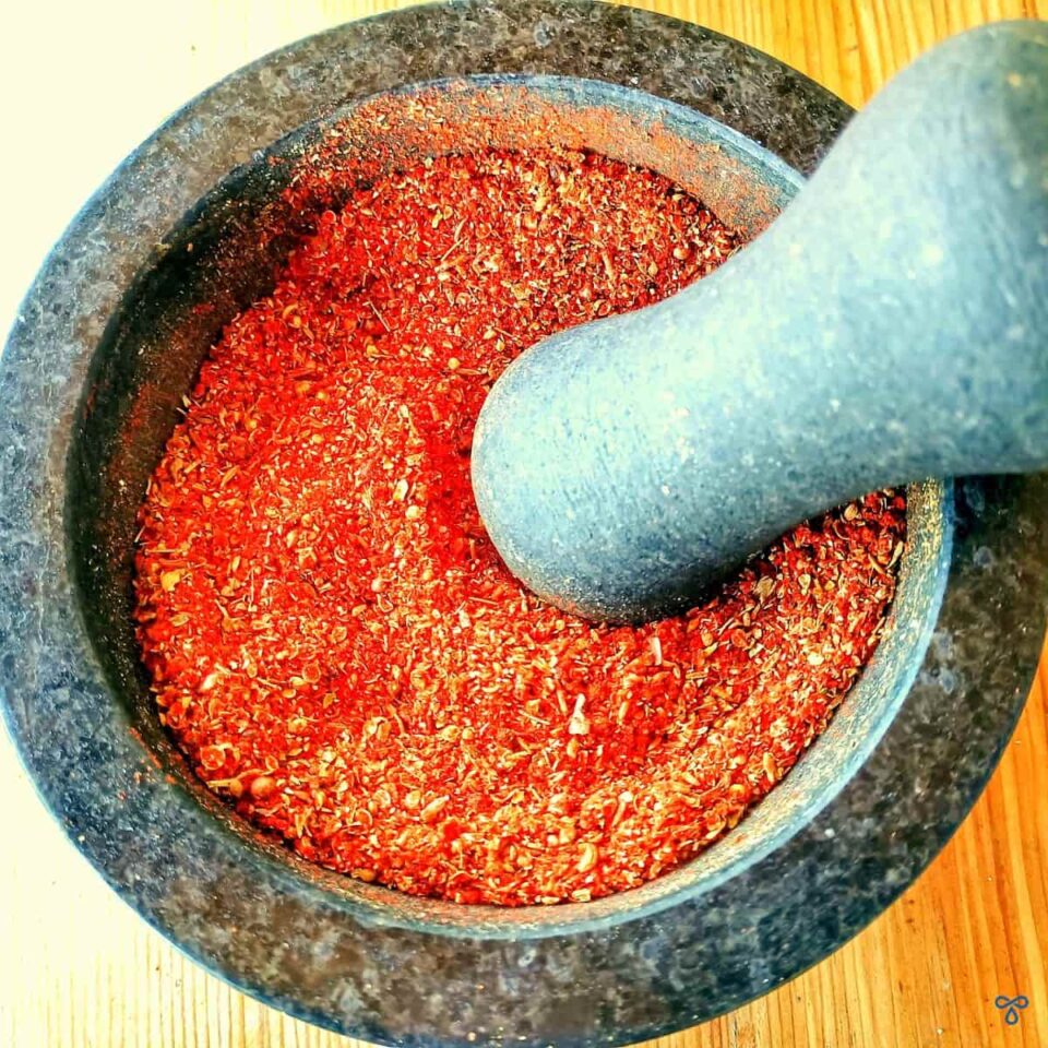 A granite pestle and mortar taken from above. It is filled with a red spice mix.