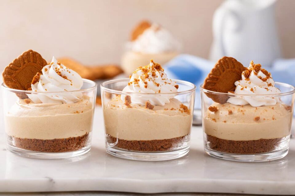 Three glass ramekins of no-bake biscoff cheesecake lined up on a marble board.